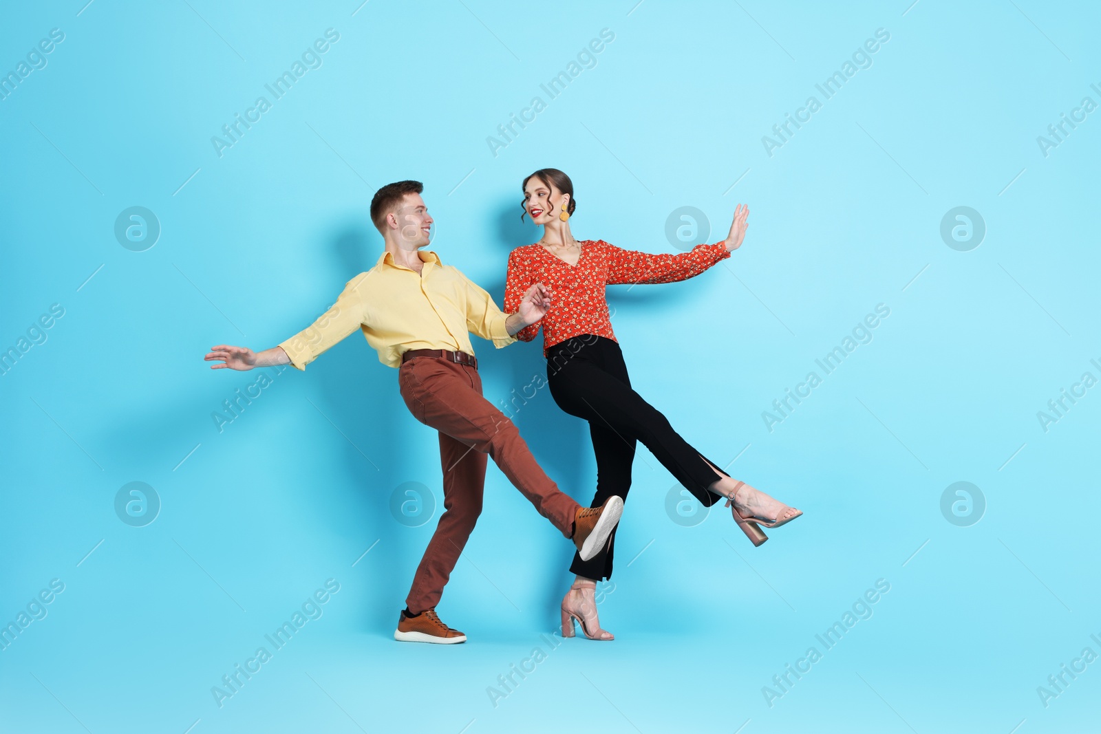 Happy couple in retro outfits dancing on light blue background Photo of Happy couple in retro outfits dancing on light blue background