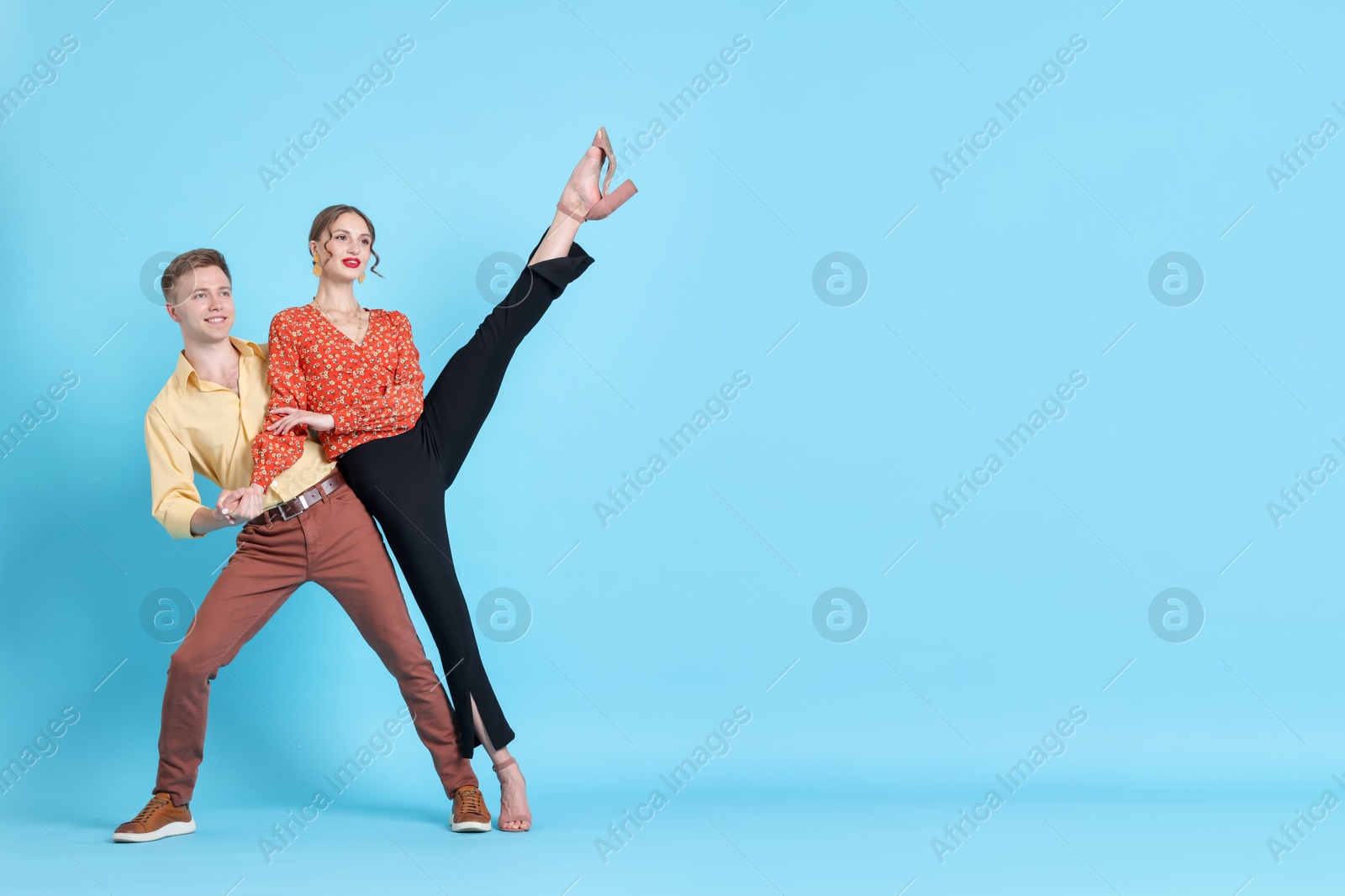 Happy couple in retro outfits dancing on light blue background, space for text Photo of Happy couple in retro outfits dancing on light blue background, space for text