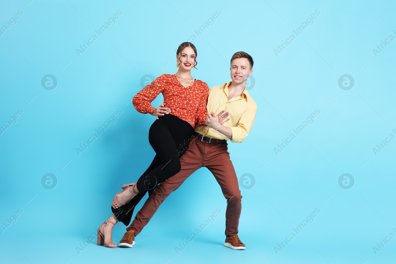 Photo of Happy couple in retro outfits dancing on light blue background