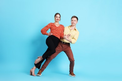 Photo of Happy couple in retro outfits dancing on light blue background