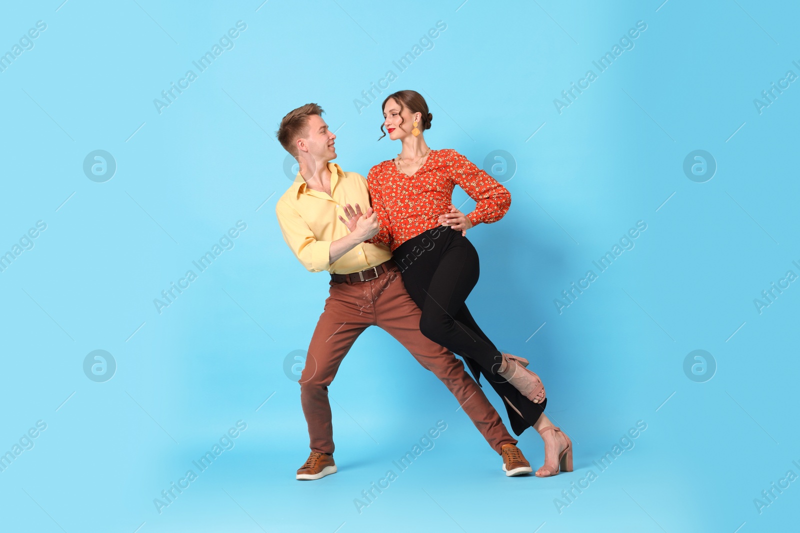 Happy couple in retro outfits dancing on light blue background Photo of Happy couple in retro outfits dancing on light blue background
