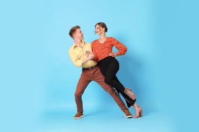 Photo of Happy couple in retro outfits dancing on light blue background