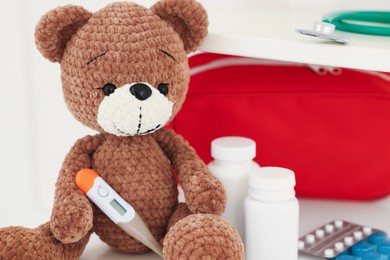 Photo of Pediatrics concept. Toy bear with thermometer and pills on white background