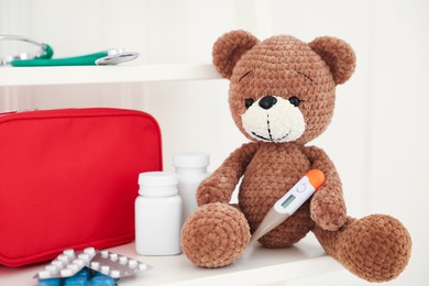 Photo of Pediatrics concept. Toy bear with thermometer and pills on white background