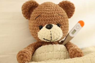 Photo of Pediatrics concept. Toy bear with thermometer in bed, closeup