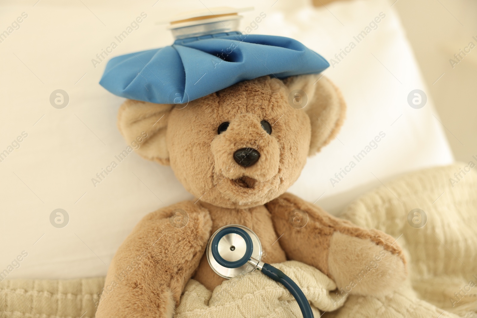 Photo of Pediatrics concept. Toy bear with ice bag and stethoscope in bed