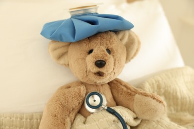 Photo of Pediatrics concept. Toy bear with ice bag and stethoscope in bed