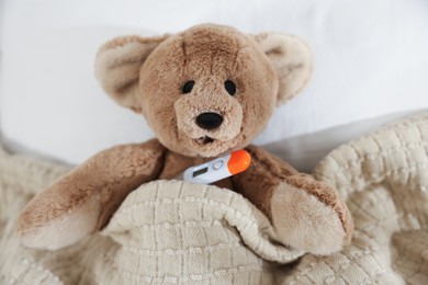 Photo of Pediatrics concept. Toy bear with thermometer in bed