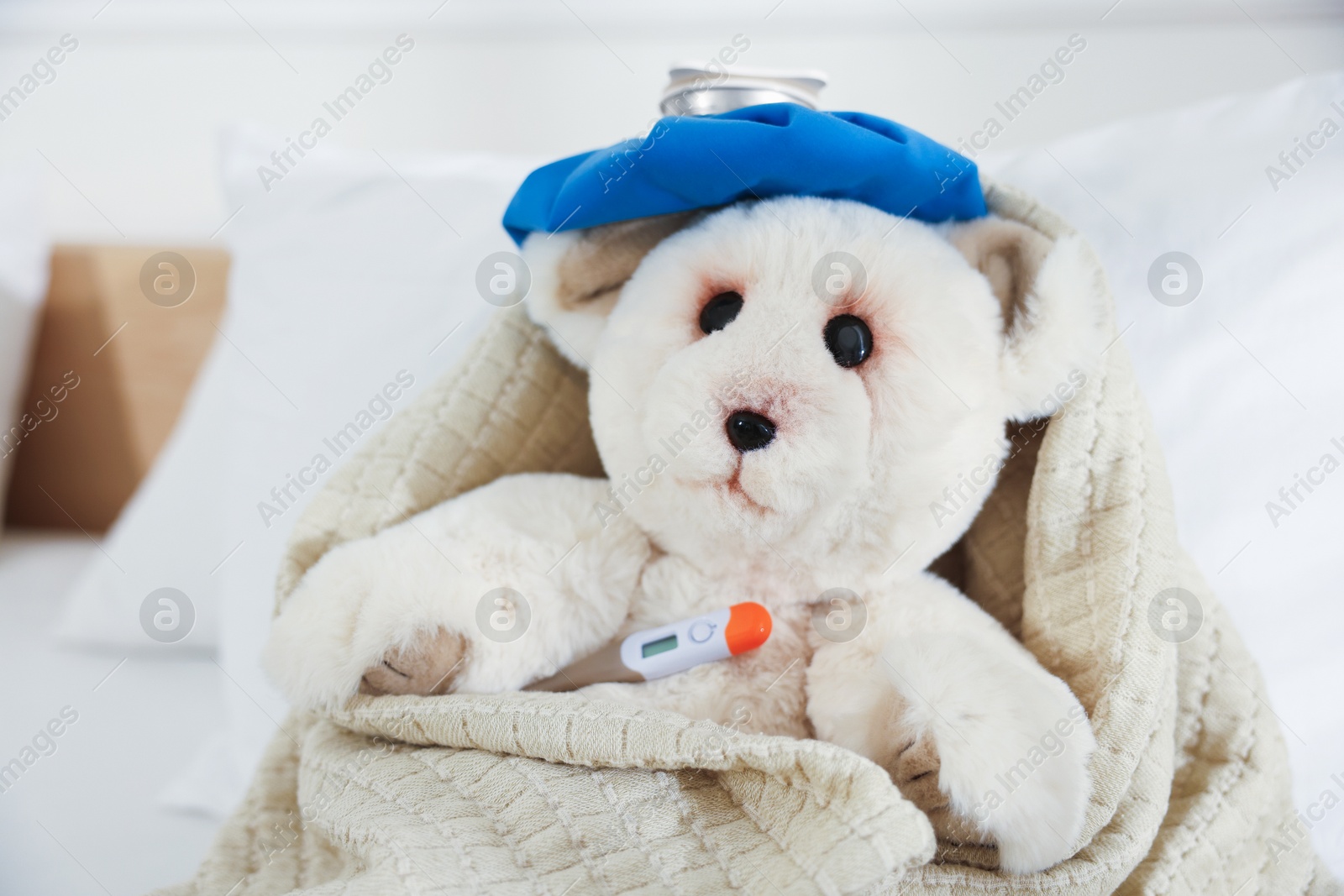Photo of Pediatrics concept. Toy bear with ice bag and thermometer in bed