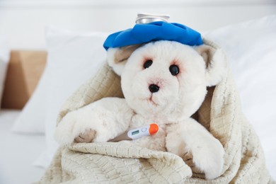 Photo of Pediatrics concept. Toy bear with ice bag and thermometer in bed