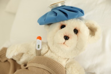 Photo of Pediatrics concept. Toy bear with ice bag and thermometer in bed