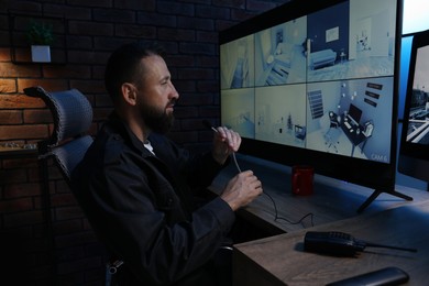 Photo of Security guard monitoring CCTV cameras and using microphone in office at night
