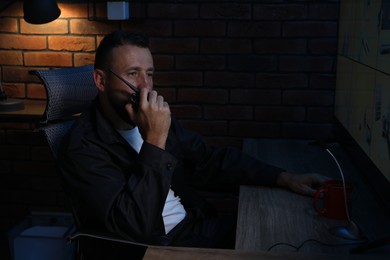 Photo of Security guard monitoring CCTV cameras and using walkie talkie in office at night
