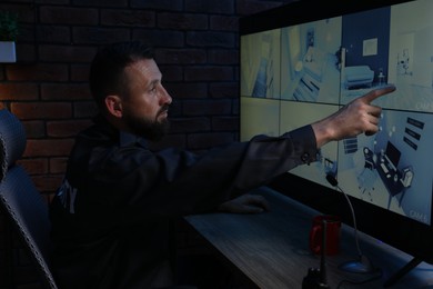 Photo of Security guard monitoring CCTV cameras in office at night