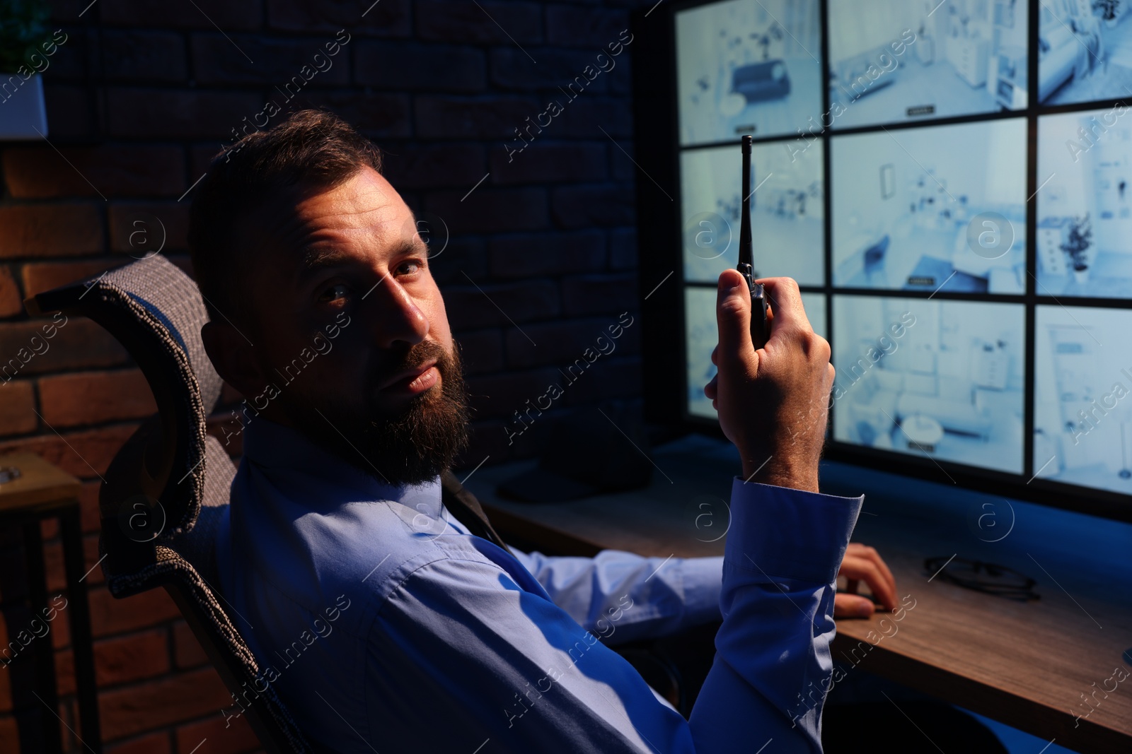 Security guard monitoring CCTV cameras and using walkie talkie in office at night Photo of Security guard monitoring CCTV cameras and using walkie talkie in office at night