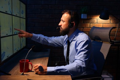 Photo of Security guard monitoring CCTV cameras in office at night