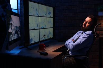Photo of Tired security guard monitoring CCTV cameras in office at night