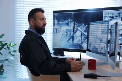 Photo of Security guard with walkie talkie monitoring CCTV cameras in office