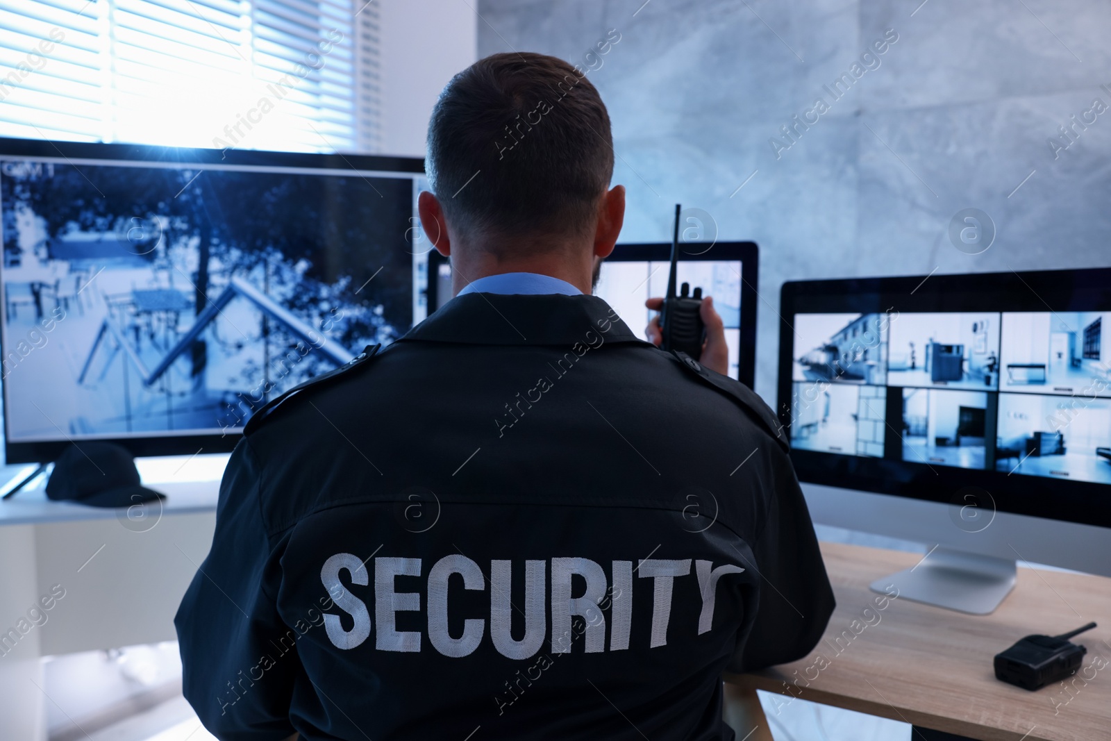 Security guard monitoring CCTV cameras and using walkie talkie in office, back view Photo of Security guard monitoring CCTV cameras and using walkie talkie in office, back view