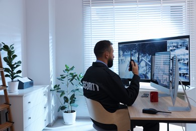 Photo of Security guard monitoring CCTV cameras in office, back view