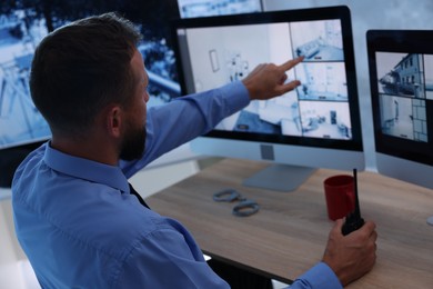 Photo of Security guard monitoring CCTV cameras in office, back view