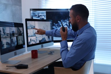 Photo of Security guard monitoring CCTV cameras and using walkie talkie in office