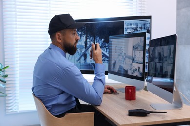 Photo of Security guard monitoring CCTV cameras and using walkie talkie in office