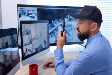 Photo of Security guard monitoring CCTV cameras and using walkie talkie in office