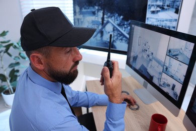 Photo of Security guard monitoring CCTV cameras and using walkie talkie in office