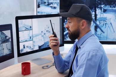 Photo of Security guard monitoring CCTV cameras and using walkie talkie in office