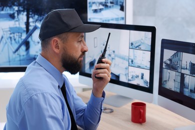 Photo of Security guard monitoring CCTV cameras and using walkie talkie in office
