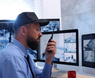Photo of Security guard monitoring CCTV cameras and using walkie talkie in office