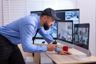 Photo of Security guard monitoring CCTV cameras and using walkie talkie in office
