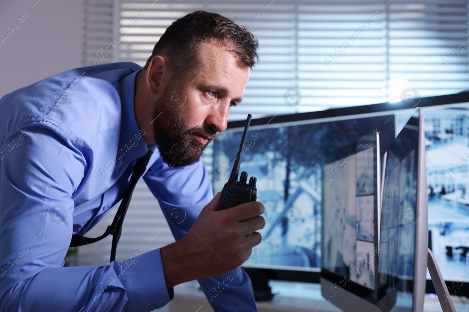 Security guard monitoring CCTV cameras and using walkie talkie in office Photo of Security guard monitoring CCTV cameras and using walkie talkie in office