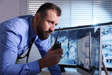 Photo of Security guard monitoring CCTV cameras and using walkie talkie in office