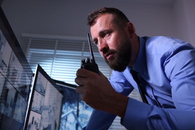 Photo of Security guard monitoring CCTV cameras and using walkie talkie in office