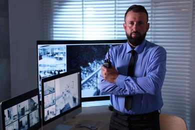 Photo of Security guard with walkie talkie near CCTV cameras in office