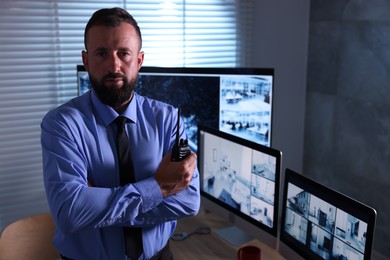 Photo of Security guard with walkie talkie near CCTV cameras in office