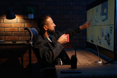 Photo of Security guard monitoring CCTV cameras in office at night