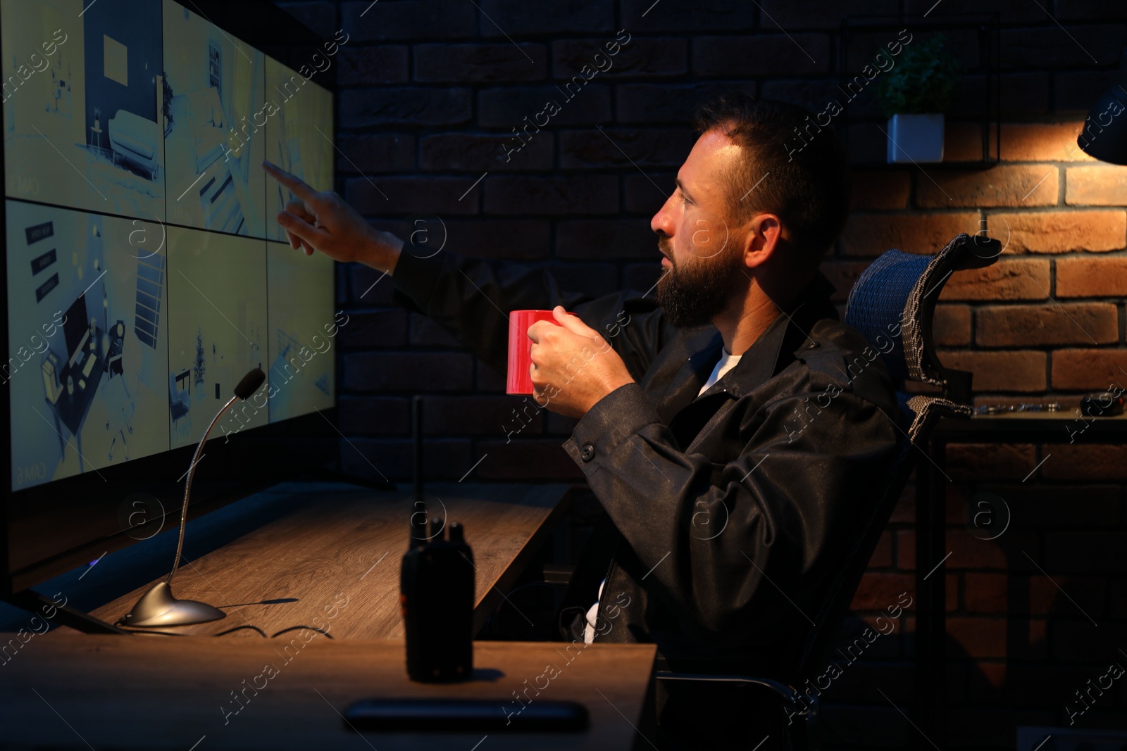 Photo of Security guard monitoring CCTV cameras in office at night