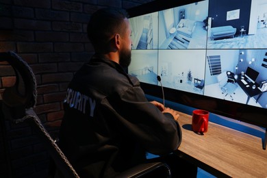 Photo of Security guard monitoring CCTV cameras in office at night, back view