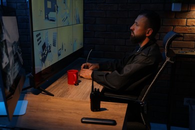 Photo of Security guard monitoring CCTV cameras in office at night