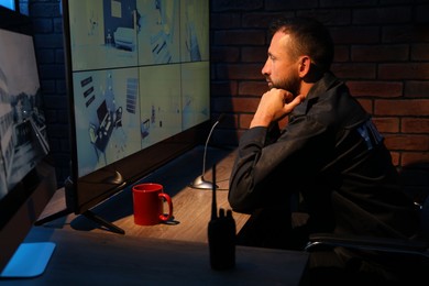 Photo of Security guard monitoring CCTV cameras in office at night