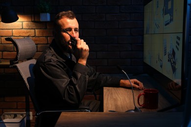 Photo of Security guard monitoring CCTV cameras and using walkie talkie in office at night