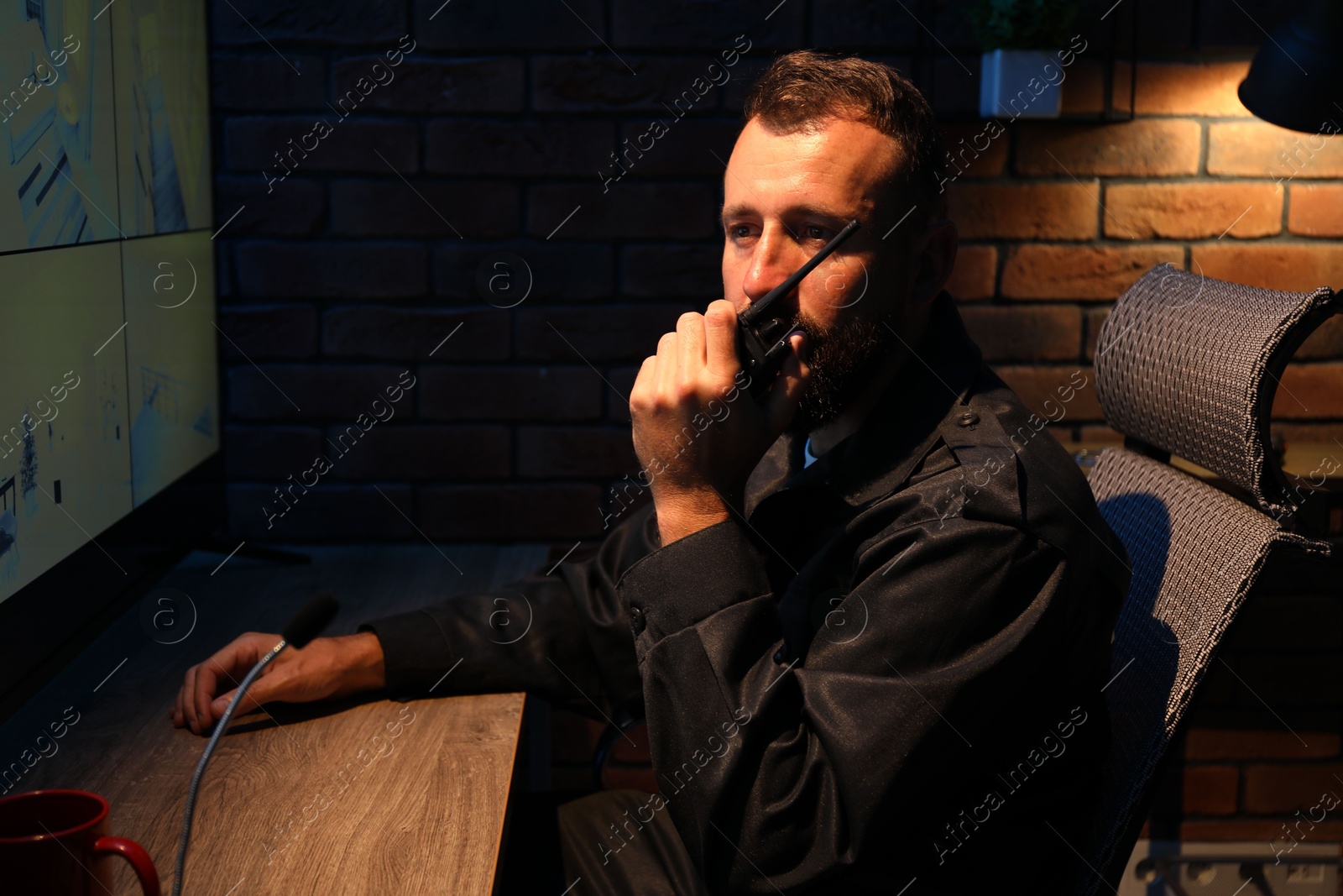 Security guard monitoring CCTV cameras and using walkie talkie in office at night Photo of Security guard monitoring CCTV cameras and using walkie talkie in office at night