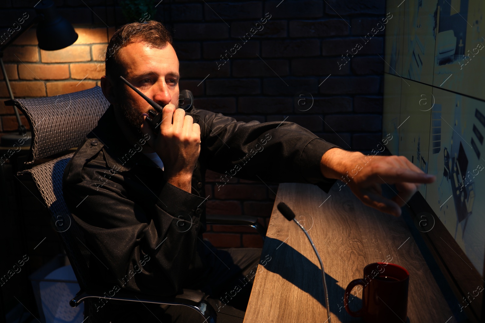 Photo of Security guard monitoring CCTV cameras and using walkie talkie in office at night