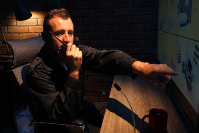 Photo of Security guard monitoring CCTV cameras and using walkie talkie in office at night