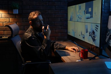 Photo of Security guard monitoring CCTV cameras and using walkie talkie in office at night