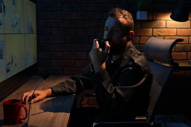 Photo of Security guard monitoring CCTV cameras and using walkie talkie in office at night