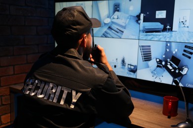 Photo of Security guard monitoring CCTV cameras in office at night, back view